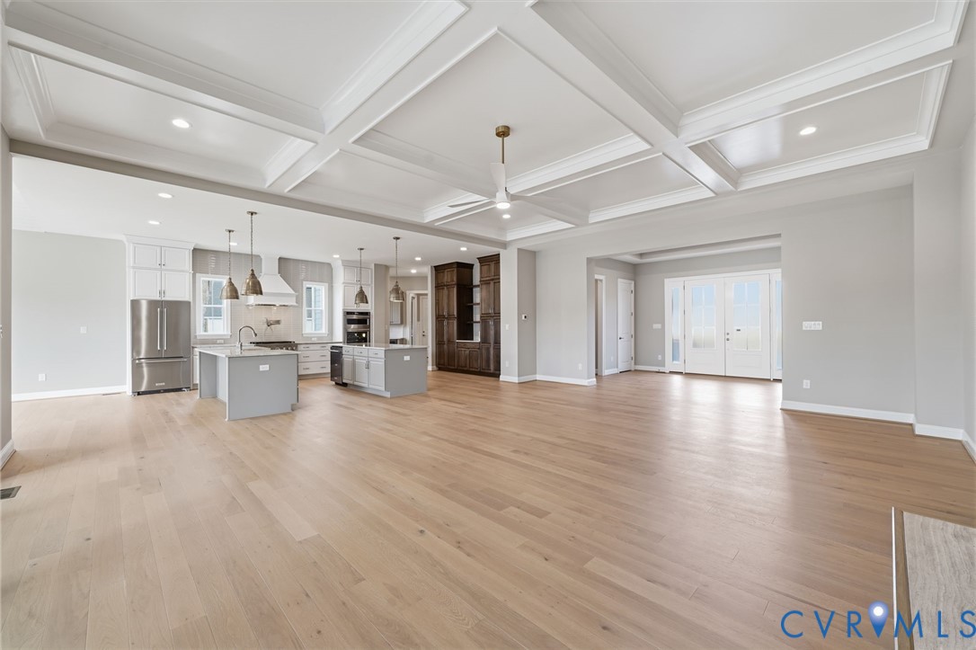 Coffered ceiling featuring recessed lighting, wood-finish flooring, central island with quartz countertops, custom cabinetry, and double French doors