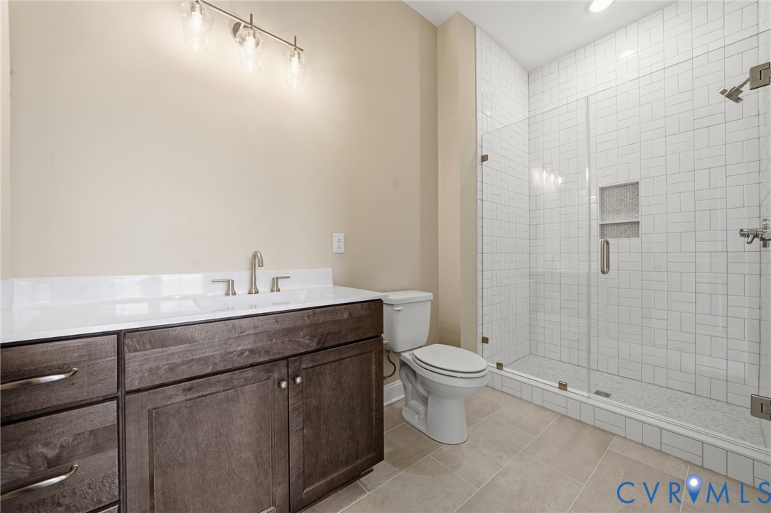 Dark-finish wood vanity with a white countertop, integrated sink, wall-mounted light fixture, and a glass-enclosed shower featuring white subway-style tile and an integrated niche