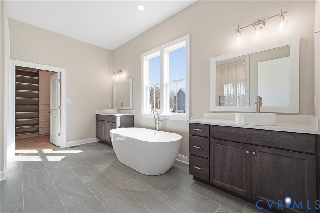 Freestanding soaking tub, dual vanities with white vessel sinks, quartz countertops, dark-finish cabinetry, and large-format tile flooring