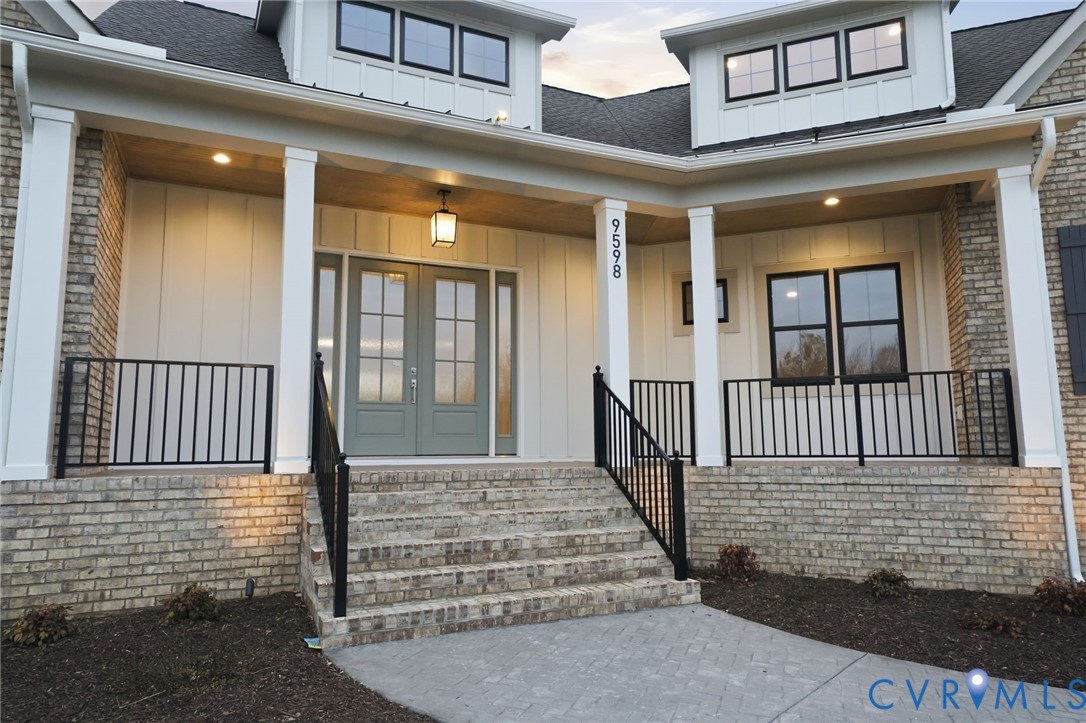 Covered entryway featuring a brick facade, board-and-batten siding, double front doors with glass paneling, and black metal railings