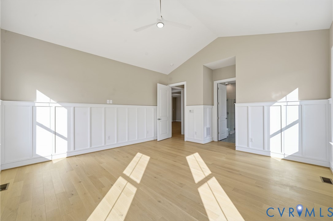 Vaulted ceiling with a central white ceiling fan, wood-finish flooring, and white wainscoting encompassing the lower walls