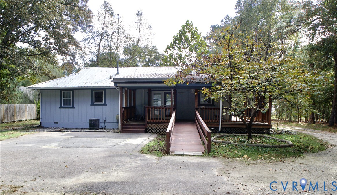 Single-story residence featuring light-toned vertical siding, a metal roof, an expansive wood-finished deck, and a dedicated ramp structure