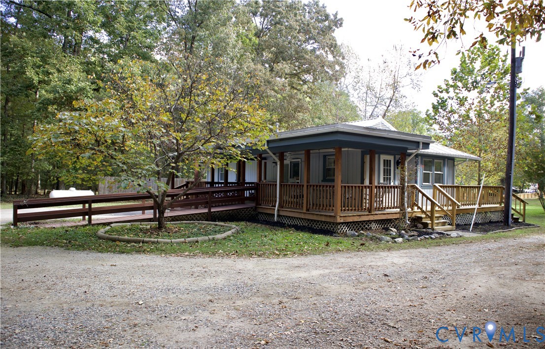 Single-story exterior featuring light-toned siding, a wrap-around wooden deck, a wooden ramp, and a metal roof
