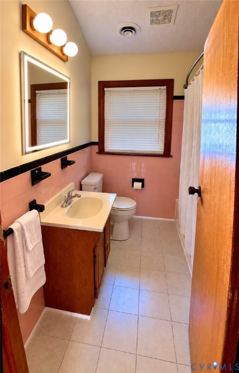 Bathroom featuring ceramic tile flooring, a wood-finish vanity with a drop-in sink, an illuminated vanity mirror, and black wall-mounted hardware
