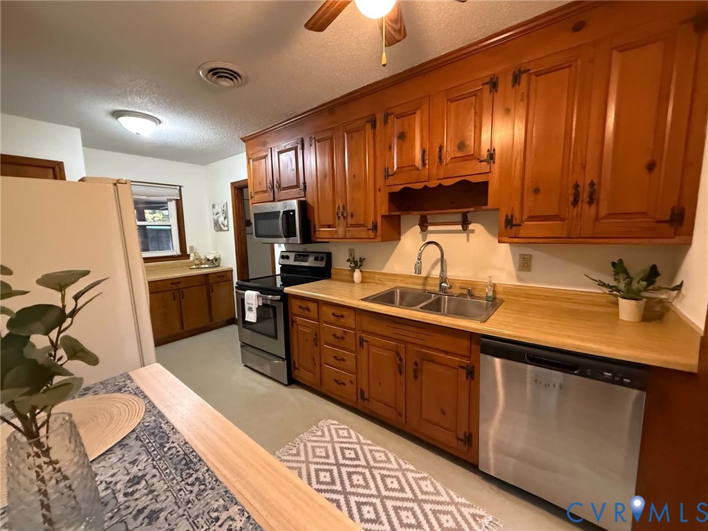 Kitchen featuring wood cabinetry, stainless steel appliances, dual-basin sink with arched faucet, and laminate countertops