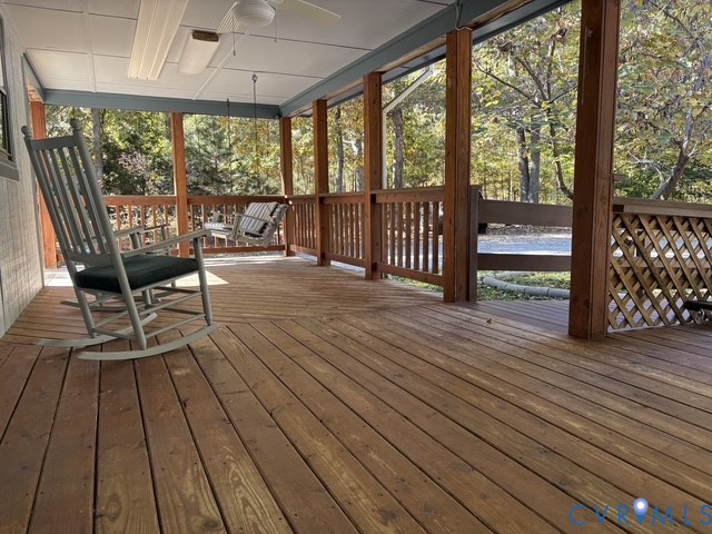Covered wooden deck featuring horizontal railings, lattice skirting, a mounted ceiling fan, and overhead lighting