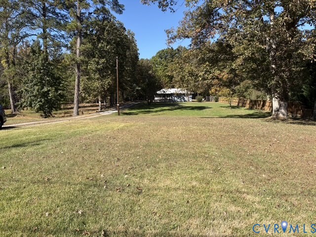 Expansive grass lawn featuring mature trees, a gravel driveway, and wood-panel fencing