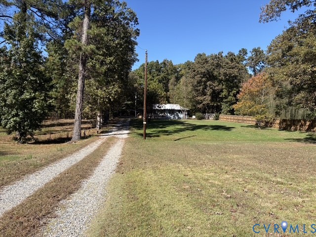Expansive lot featuring a gravel drive, manicured lawn, perimeter wood fencing, and mature trees