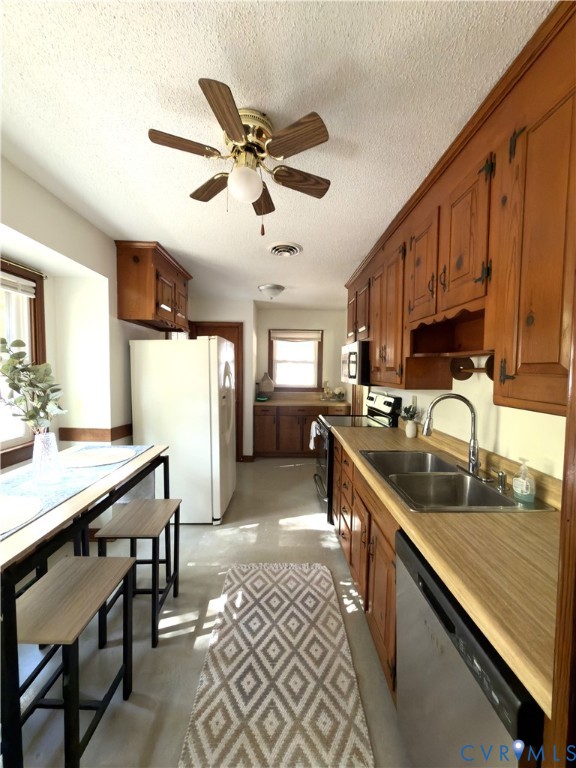 Kitchen featuring natural wood cabinetry, laminate countertops, dual-basin stainless steel sink with pull-down faucet, and built-in stainless steel dishwasher