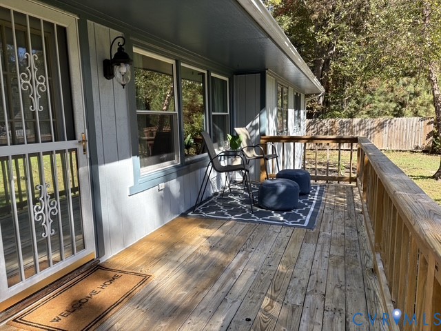 Covered exterior deck featuring wood decking, wood railing, vertical siding, and a decorative metal storm door