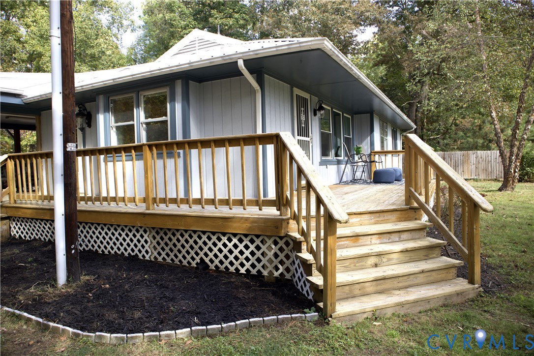 Exterior featuring wood-tone decking with stairs, lattice skirting, vertical siding, and a metal roof
