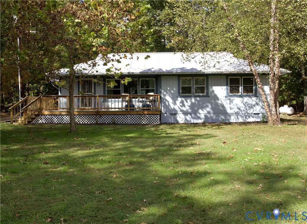 Single-story exterior featuring light-toned vertical siding, a metal roof, an expansive wood deck, and decorative lattice skirting Single-story exterior featuring light-toned vertical siding, a metal roof, an expansive wood deck, and decorative lattice skirting