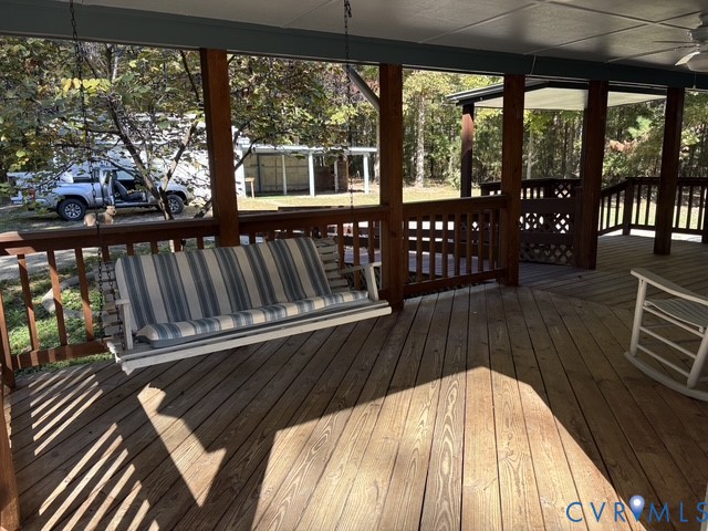 Covered wood deck featuring a built-in porch swing, wood railing, lattice accents, and a ceiling fan
