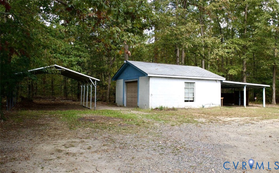 Detached outbuilding featuring a white brick exterior, pitched roof, single-bay garage, and two integrated metal-frame carports