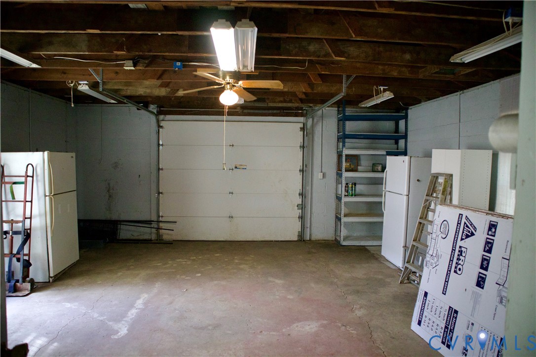 Garage featuring exposed joist ceiling, concrete flooring, overhead lighting, ceiling fan, and built-in metal shelving