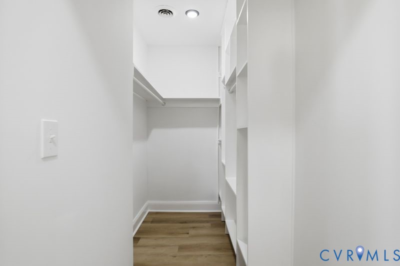 Walk-in closet featuring white built-in shelving, integrated hanging rods, and wood-finish flooring