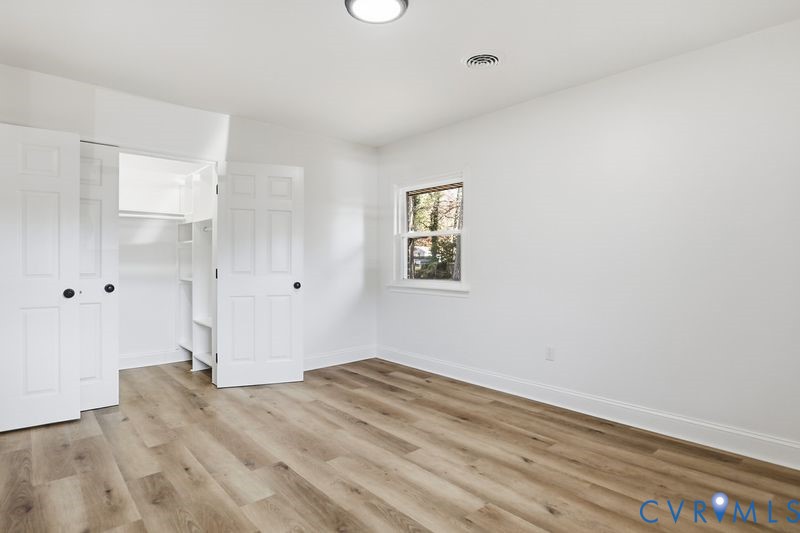 Neutral interior featuring wood-finish flooring, a single window, and a closet with double-panel doors and built-in shelving