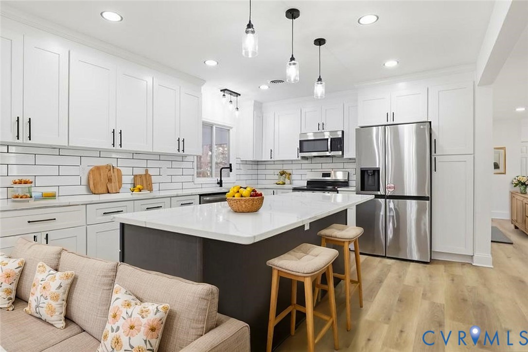 Kitchen featuring white shaker-style cabinetry, a central island with a stone-surface countertop, white subway tile backsplash, stainless steel appliances, and wood-finish flooring