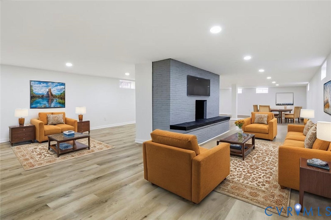Open-concept living space featuring wood-finish flooring, recessed lighting, and a prominent floor-to-ceiling brick fireplace with a raised hearth