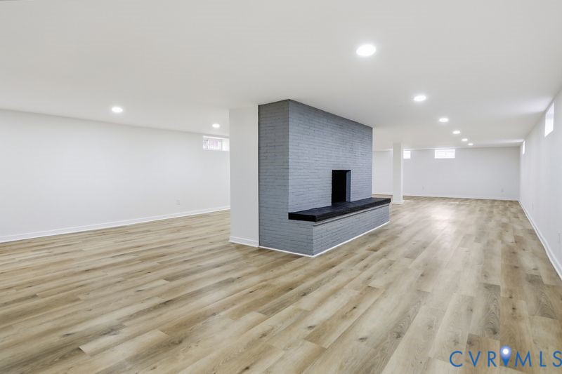 Open-concept interior featuring wood-finish flooring, recessed lighting, and a central floor-to-ceiling painted brick fireplace with a built-in hearth