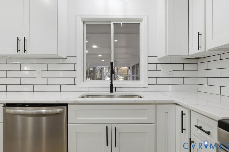 White shaker-style cabinetry with matte black hardware, stone-finish countertops, subway tile backsplash, stainless steel dishwasher, and a gooseneck faucet