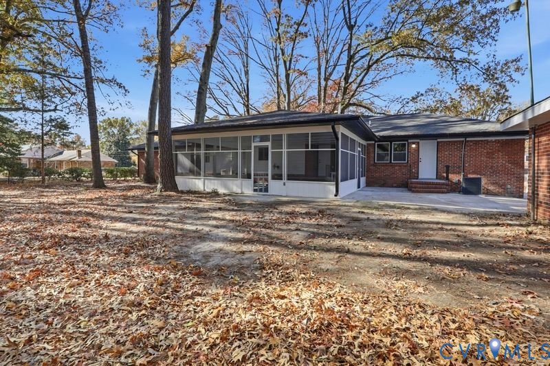 Red brick exterior featuring a white-framed screened-in porch, concrete patio, and mature trees