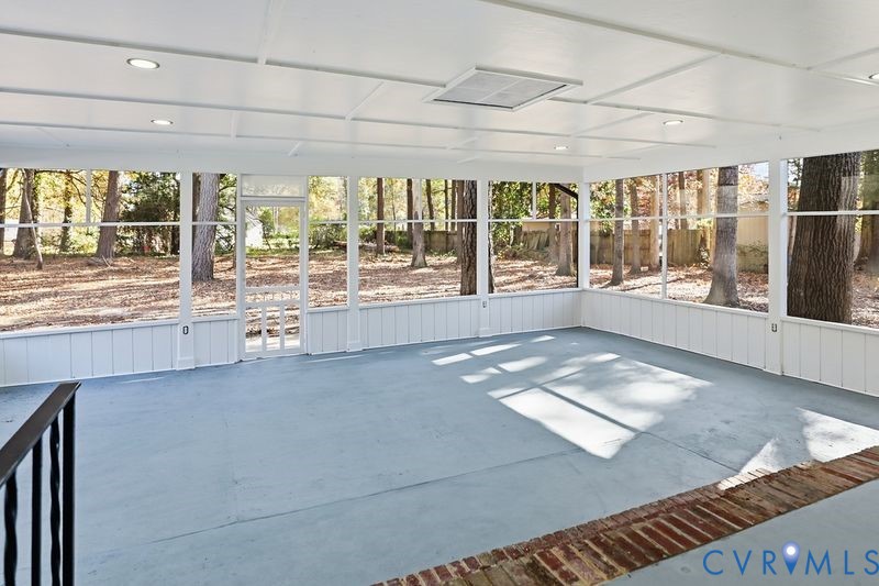 Enclosed porch featuring a painted concrete floor, white-paneled walls, ceiling-mounted recessed lighting, and expansive screened windows