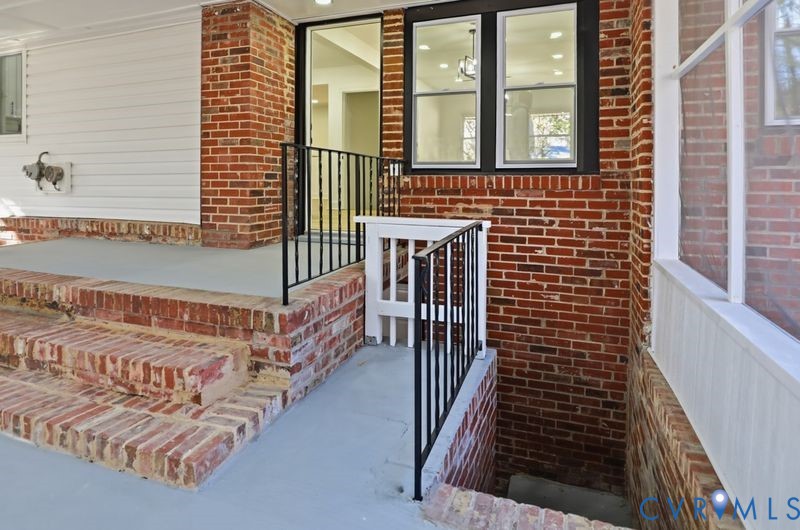 Multi-level brick exterior staircase featuring smooth-finished concrete steps, black metal handrails, and white paneled siding