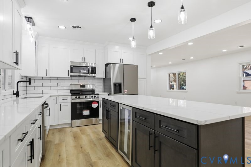 Kitchen featuring white shaker-style cabinetry, a contrasting dark-toned center island with a built-in beverage refrigerator, stone-surface countertops, subway tile backsplash, and stainless steel appliances