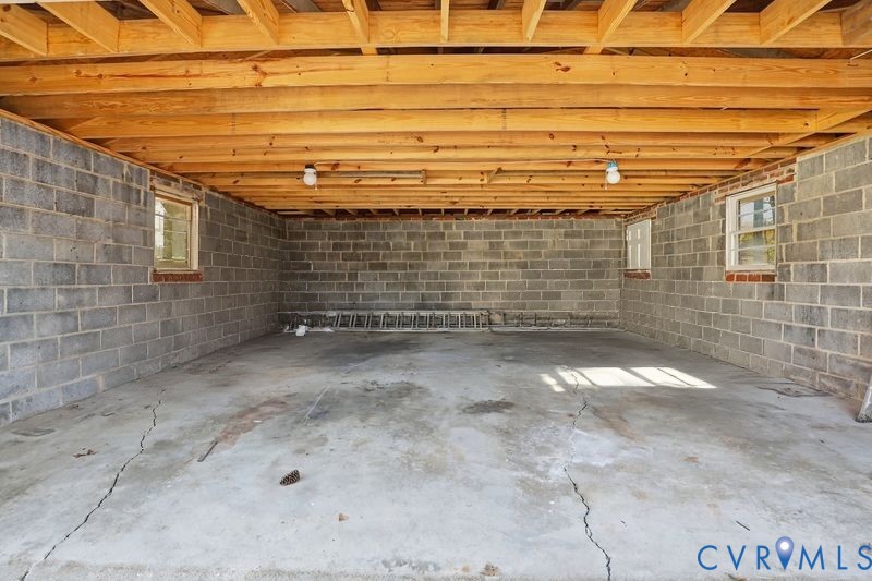 Unfinished lower-level space featuring exposed timber joist ceiling, concrete block walls, and concrete flooring, punctuated by multiple inset windows