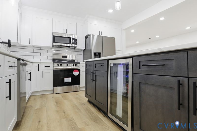 Kitchen featuring white upper cabinetry, dark-finish lower island cabinetry, stainless steel appliances, a built-in beverage refrigerator, and wood-finish flooring