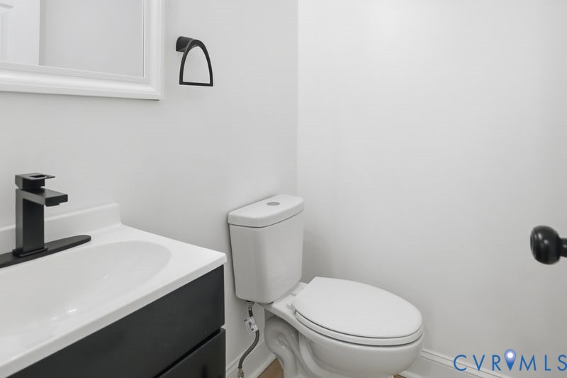 Bathroom featuring a vanity with dark cabinetry and a white countertop, matte black single-handle faucet, white toilet, and geometric wall-mounted hardware