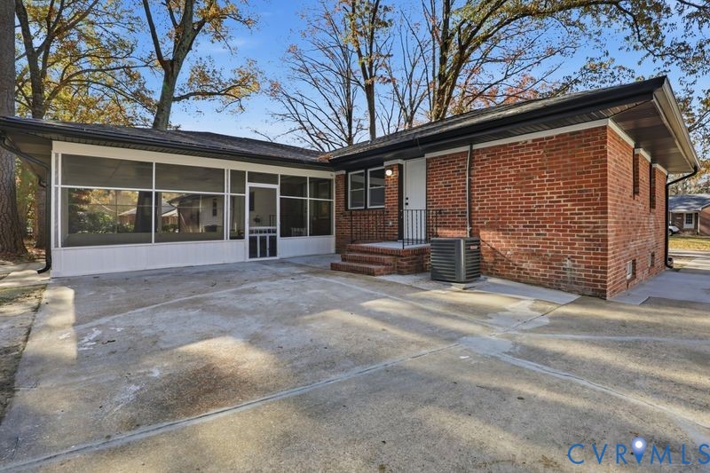 Red brick exterior featuring a screened-in porch, concrete patio, and mature trees