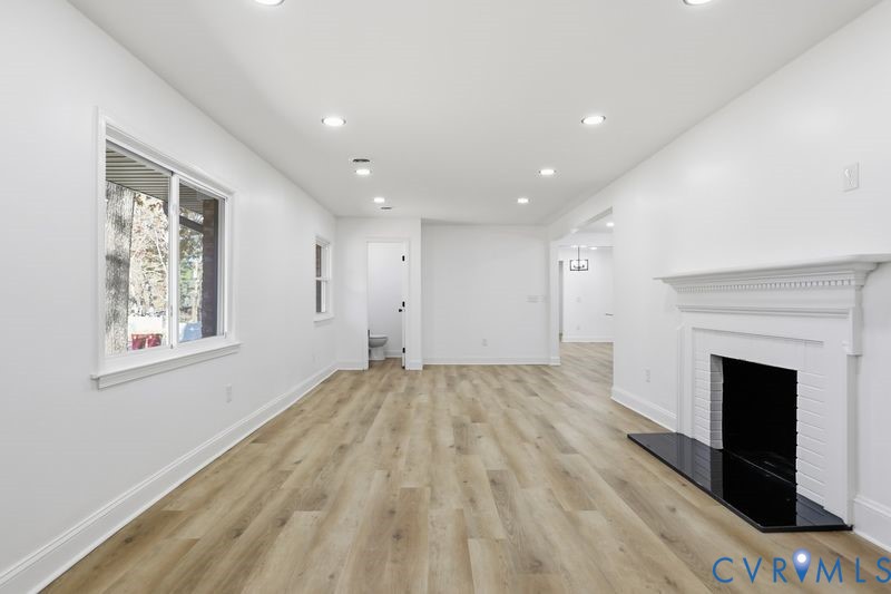 Open-concept room featuring wood-finish flooring, recessed lighting, and a white fireplace mantel with a black hearth