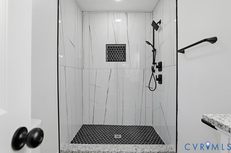 Walk-in shower featuring white large-format wall tile with contrasting veining, matte black fixtures, integrated hexagonal tile niche, and a contrasting dark hexagonal floor tile