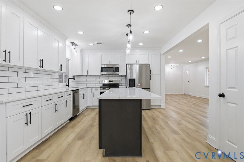 Kitchen featuring white shaker-style cabinetry, a central island with a contrasting dark base, stone-surface countertops, a subway tile backsplash, and stainless steel appliances