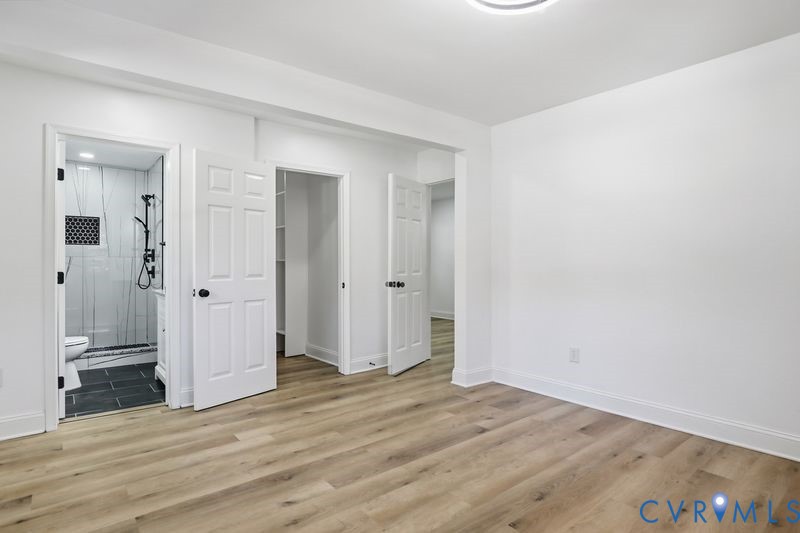 Wood-finish flooring, multi-panel interior doors, recessed ceiling lighting, and a bathroom featuring a glass-enclosed shower with dark tile flooring and wall accents