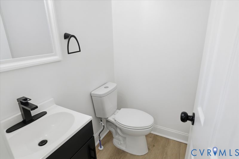 Vanity with integrated sink, matte black single-handle faucet, rectangular wall-mounted mirror, two-piece toilet, and wood-finish flooring