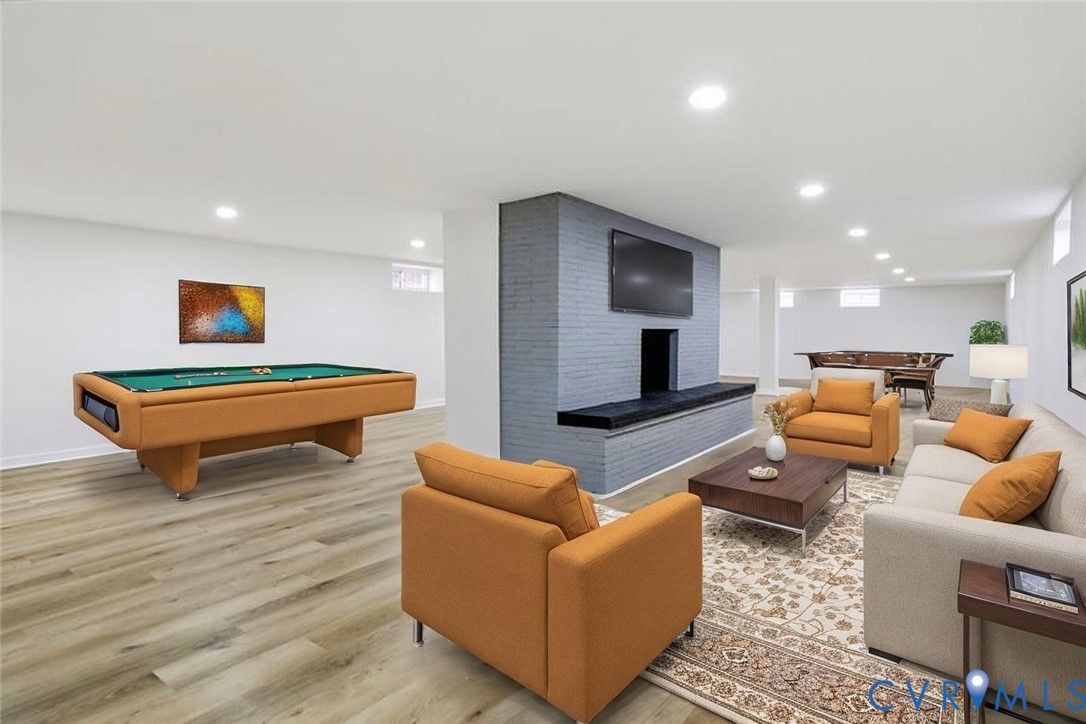 Open-concept space featuring wood-finish flooring, recessed lighting, and a dual-sided painted brick fireplace with a built-in hearth