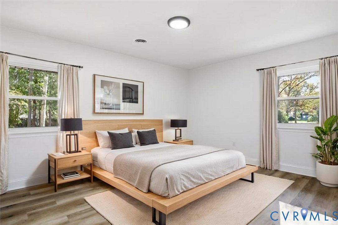 Neutral-toned room featuring wood-finish flooring, dual windows with decorative rods, and a central flush-mount ceiling light fixture