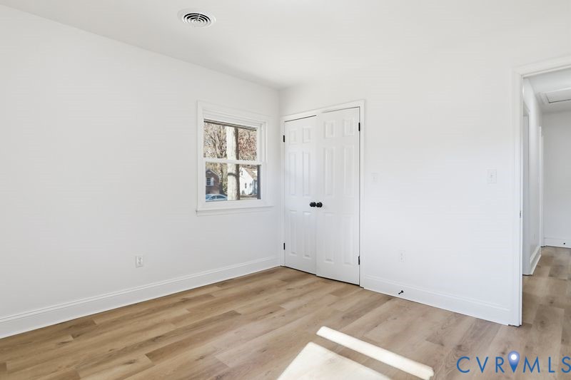 Room featuring wood-finish flooring, white walls, dual-panel closet doors with matte black hardware, and a single-hung window