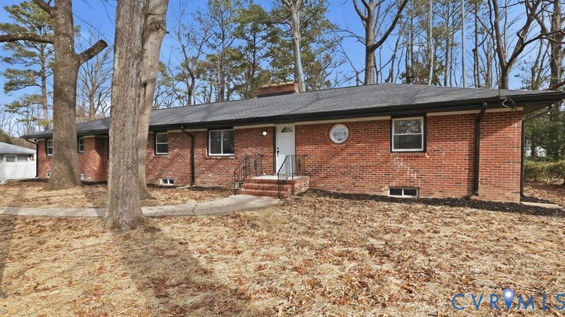 Single-story brick exterior featuring a multi-pitched roof, a central brick chimney, a circular accent window, and a concrete walkway