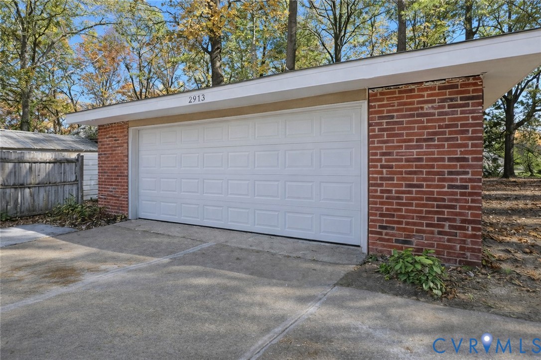 Detached two-car garage featuring a red brick exterior, a white sectional garage door, a flat roofline, and a concrete driveway