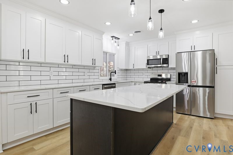 Kitchen featuring white shaker-style cabinetry, quartz countertops with an integrated central island, subway tile backsplash, stainless steel appliances, and wood-finish flooring