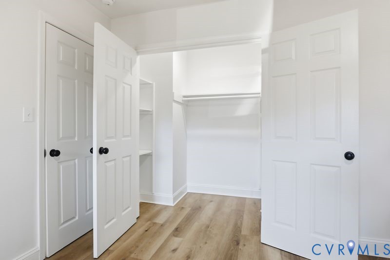Walk-in closet featuring wood-finish flooring, white six-panel doors, matte black hardware, and built-in shelving