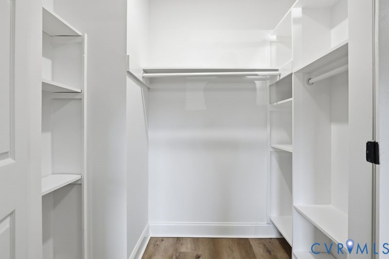 Walk-in closet featuring white built-in shelving, integrated hanging rods, and wood-finish flooring