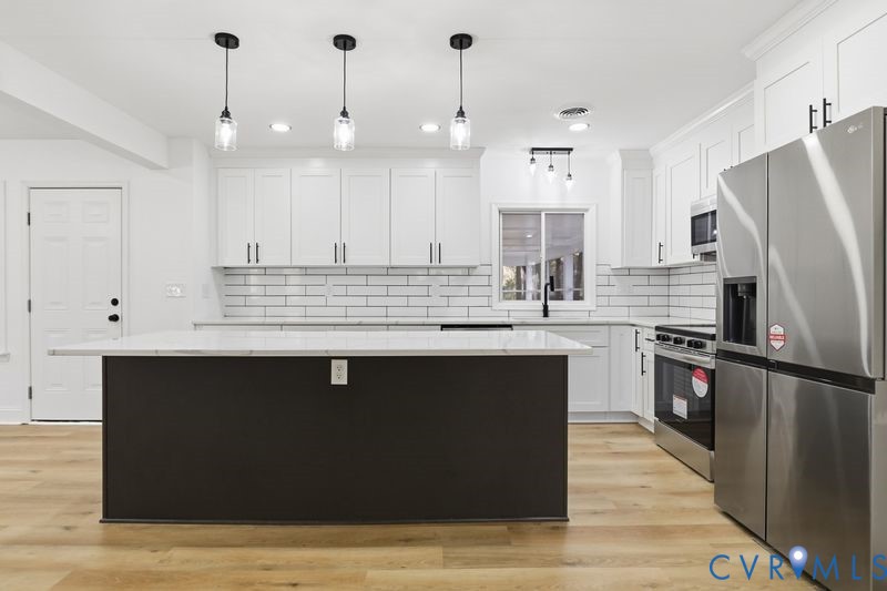Kitchen featuring white shaker-style cabinetry, white subway tile backsplash, a central island with a stone-finish countertop, stainless steel appliances, and wood-finish flooring
