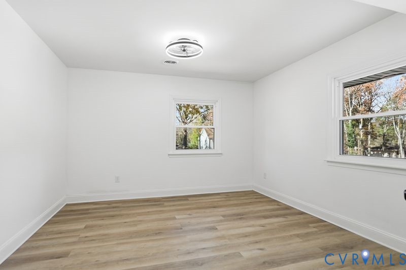 Neutral-toned room featuring wood-finish flooring, dual-pane windows, and a modern circular flush-mount ceiling light fixture