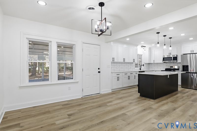 Open kitchen featuring a center island with a stone countertop, white cabinetry, subway tile backsplash, stainless steel appliances, and wood-finish flooring