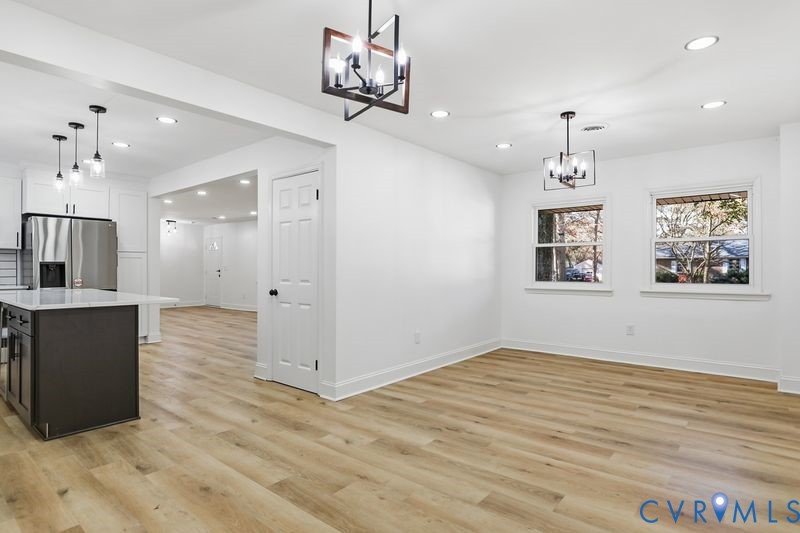 Wood-finish flooring, geometric-frame light fixtures, recessed ceiling lighting, kitchen island with stone-surface countertop, and stainless steel built-in appliances